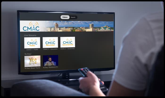 A custom-branded OTT streaming app for a local station shown on a living-room television.