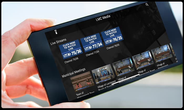 A phone showing a station's streaming app with live channels and municipal meeting VOD.