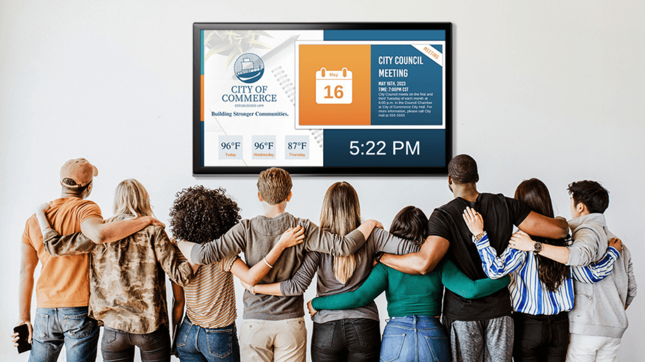 A group of people embracing each other while looking at a TV screen with a city's public announcements