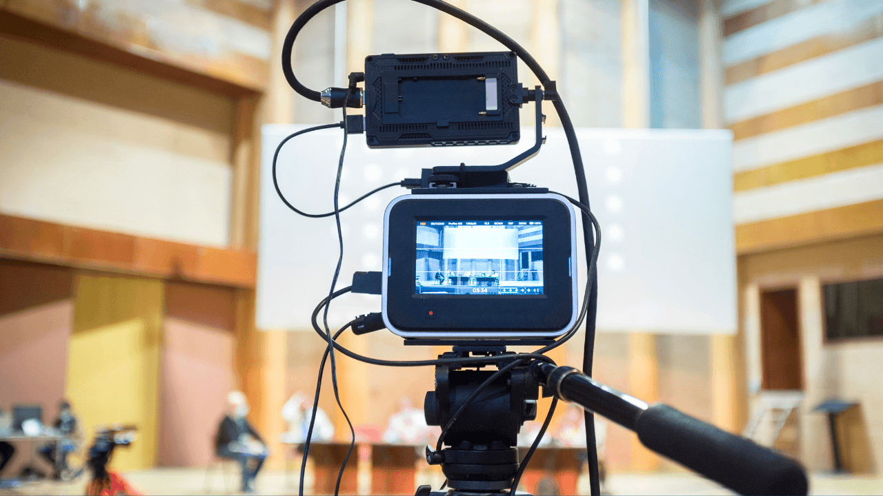 A professional film camera set up at a city council meeting for live streaming on multiple platforms